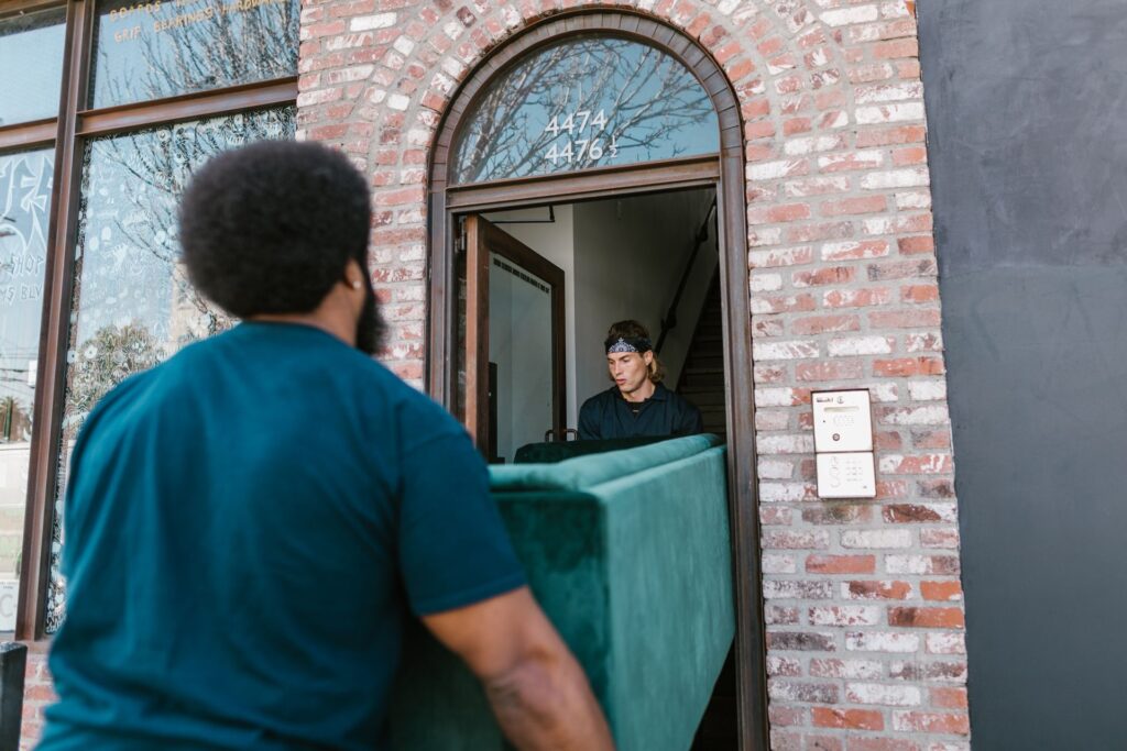 Two men carrying a green sofa through a front door